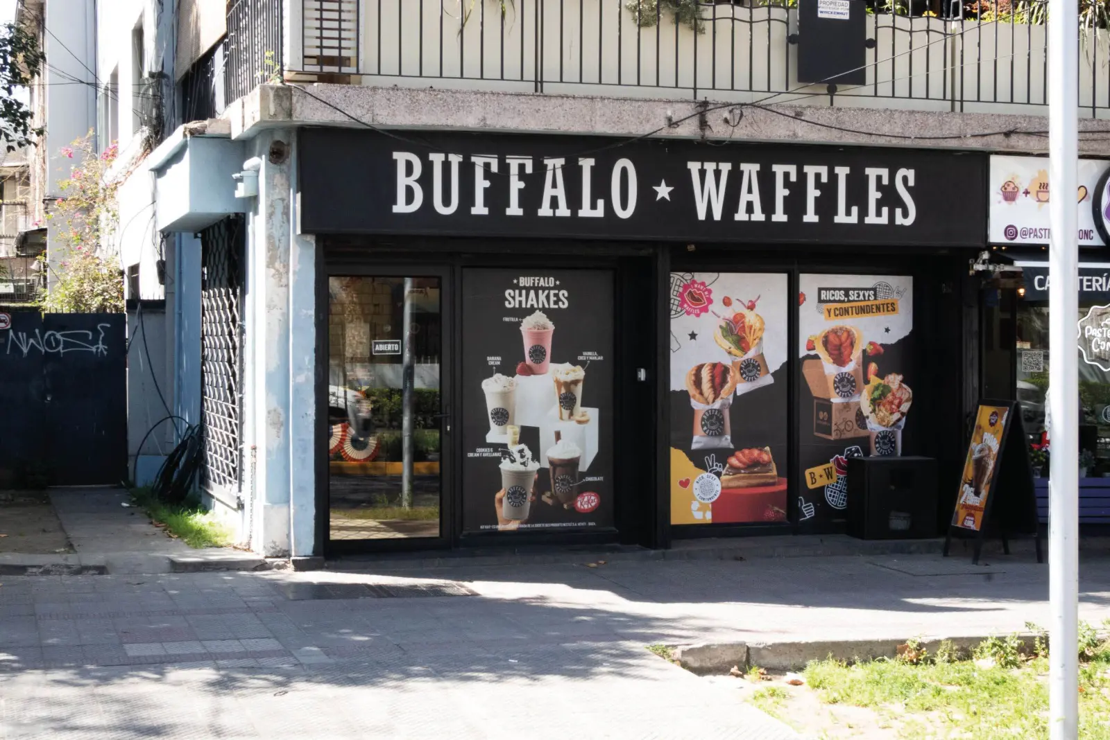 Fachada de un local Buffalo Waffles a la calle, con letrero negro y vitrinas con afiches de producto